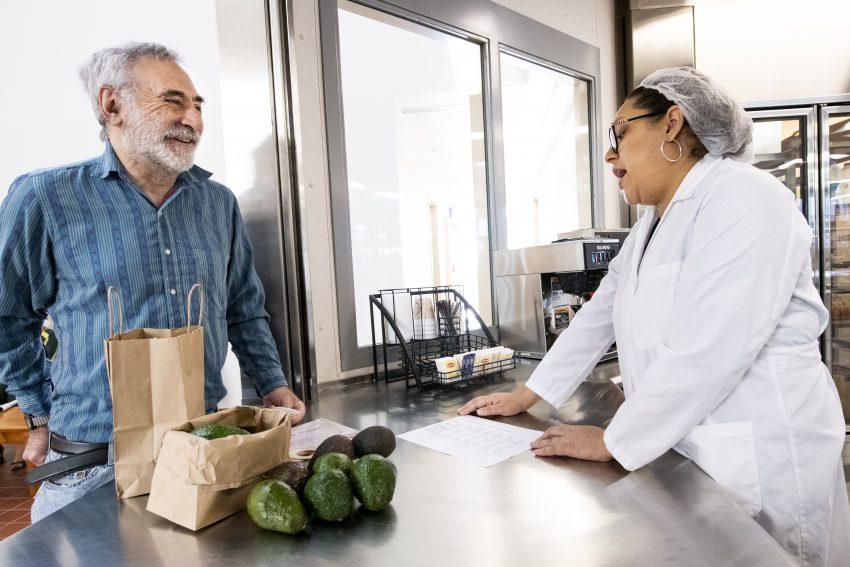 Woman in lab coat talking with man who has bags of avocados
